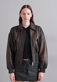 Braune Leder-Bomberjacke mit gerippten Bündchen und Saum, ausgestattet mit einem Reißverschluss vorne, schrägen Taschen und einem gesteppte Design an den Seiten.