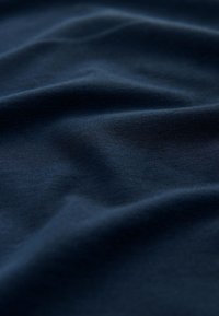 Tissu bleu foncé avec des plis doux et une texture lisse créant des ombres douces et des reflets sur toute la surface.