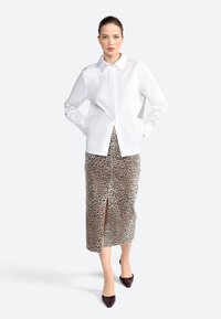 Chemise blanche à manches longues avec un col, associée à une jupe midi imprimée léopard avec une fente devant, complétée par des chaussures noires à bouts pointus.