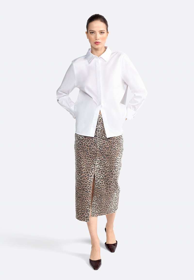 Chemise blanche à manches longues avec un col, associée à une jupe midi imprimée léopard avec une fente devant, complétée par des chaussures noires à bouts pointus.