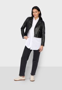 Černá kožená zkrácená bunda se zipem vepředu, v kombinaci s bílou košilí s knoflíky, černými džíny a světlými béžovými teniskami.