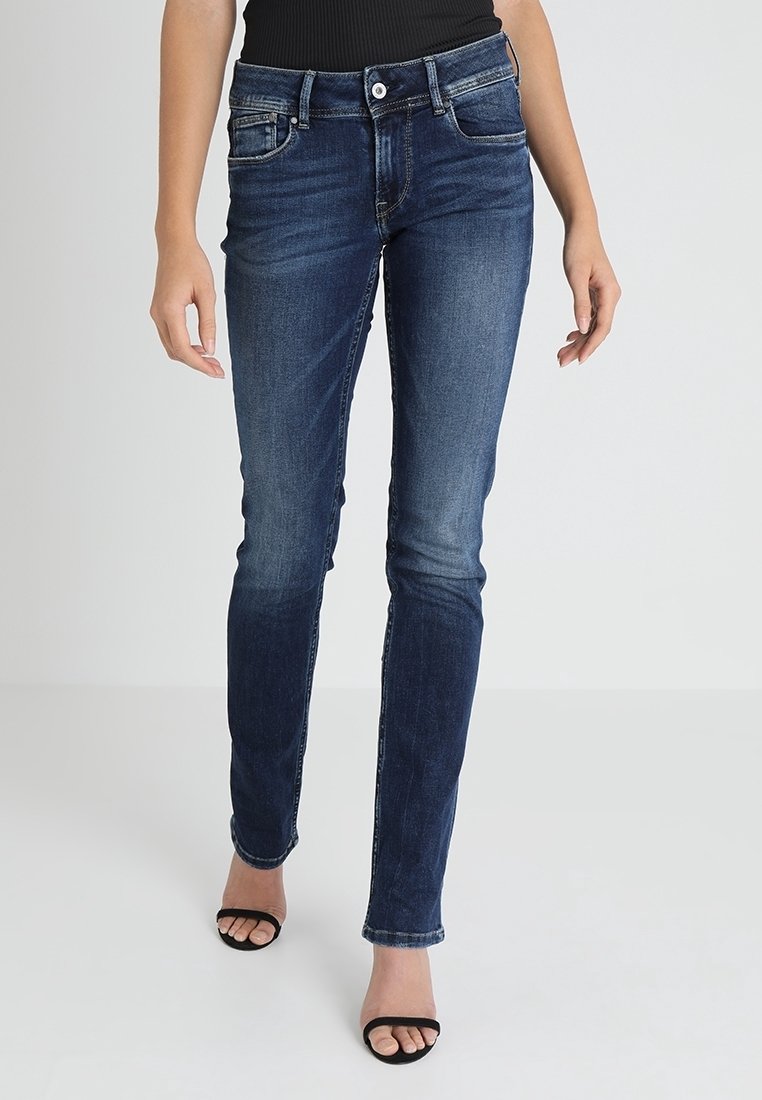 Jeans de mezclilla de lavado oscuro con un ajuste slim, diseño de cinco bolsillos, ligero desgaste en los muslos y cierre clásico de botones.