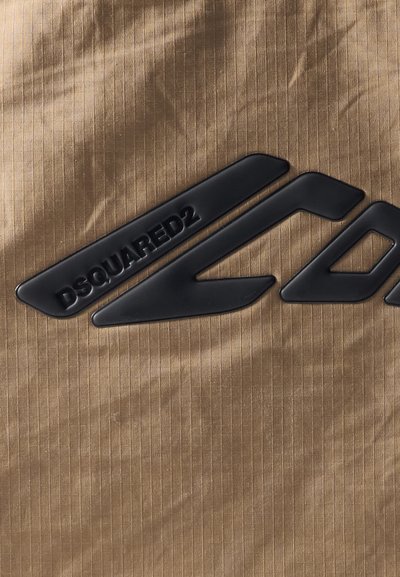 Brown fabric with a subtle ribbed texture featuring a prominent black rubber logo "DSQUARED2" and dynamic arrow-like shapes.
