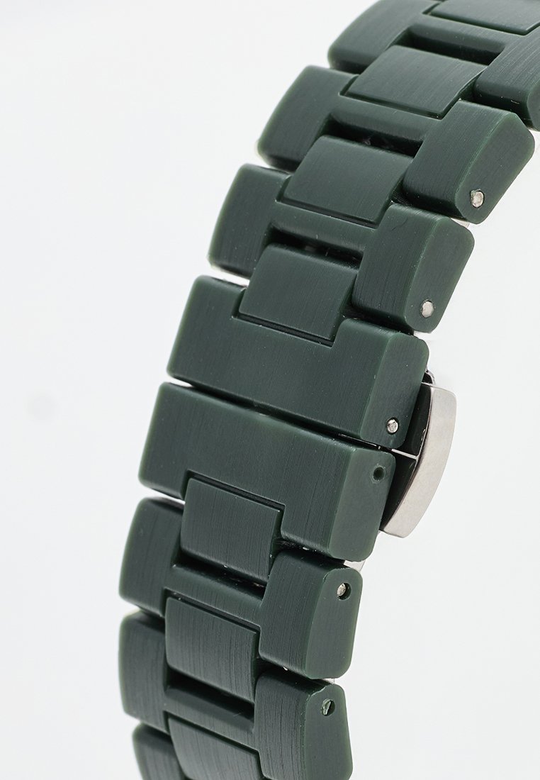 Correa de reloj de silicona verde con eslabones rectangulares, que presenta una textura cepillada y un detalle de cierre plateado. El acabado suave realza la durabilidad.