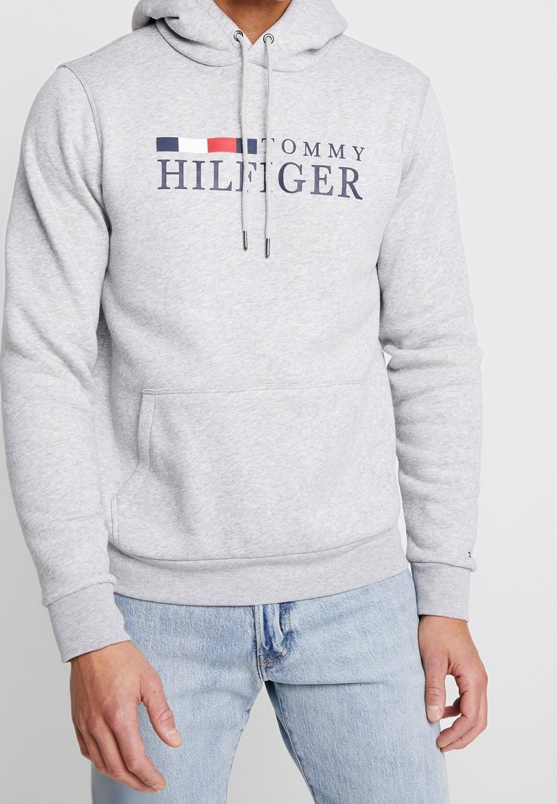 Sudadera gris de mezcla de algodón, con un bolsillo frontal, capucha con cordón y logo de "TOMMY HILFIGER" en color marino con rayas rojas y azules.