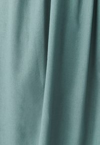 Teal kangas, jossa on pehmeä rakenne, esittelee hienovaraisia taitoksia ja sileää pintaa. Materiaali vaikuttaa kevyeltä ja hieman kiilt�ävältä.