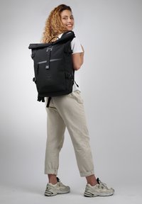 Zaino roll-top nero con spallacci regolabili, tasca frontale con zip, patch con logo e materiale resistente all'acqua. Finitura testurizzata.