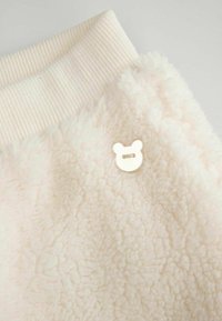 Polarowa bluza w kolorze ecru, z prążkowanym kołnierzem i małym, w kształcie misia, guzikiem jako akcentem. Miękka, teksturowana tkanina.
