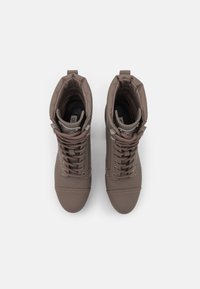 Bottes basses imperméables marron avec texture lisse, design à lacets, col rembourré et embout renforcé. Intérieur doublé et semelle en caoutchouc.