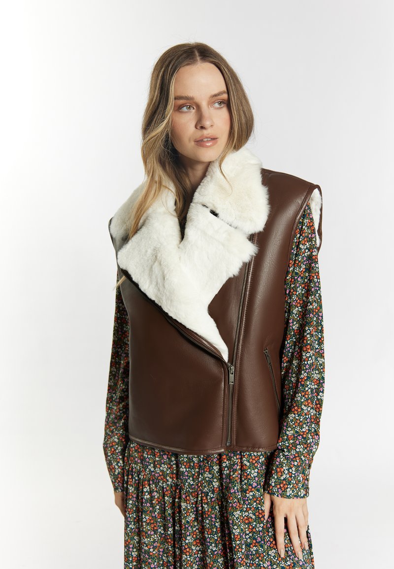 Bruine leren vest met een witte faux fur kraag en rits, gelaagd over een bloemenpatroon jurk met lange mouwen en een geplooide rok.