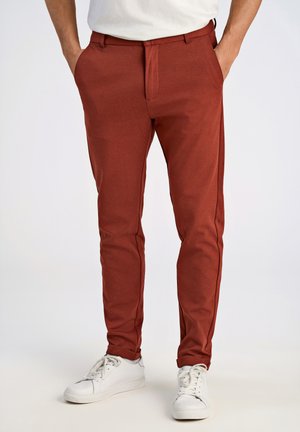 Pantalones de tela elástica rojos con un ajuste slim, que cuentan con bolsillos laterales y pierna recta, combinados con zapatillas blancas.