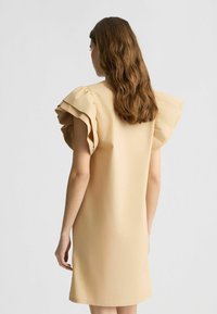 Abito corto beige con maniche arricciate, realizzato in tessuto liscio, caratterizzato da una silhouette rilassata e una lunghezza fino al ginocchio.