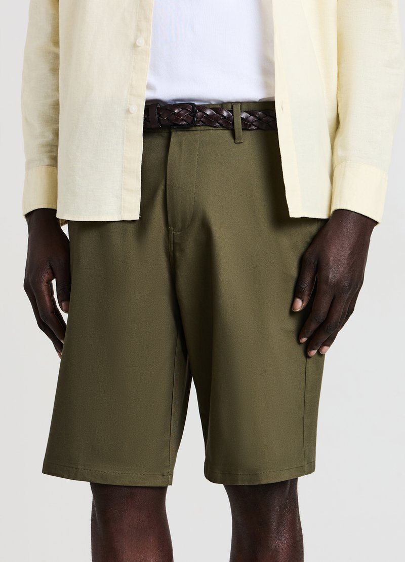 Olive green shorts with a smooth texture and tailored fit, paired with a light beige linen shirt and a braided brown leather belt.
