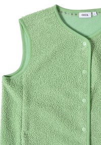 Grön ärmlös väst i textil med strukturerad yta, som har en mjuk och fluffig yta, rund halsringning och tryckknappsstängning. Lappen är synlig.