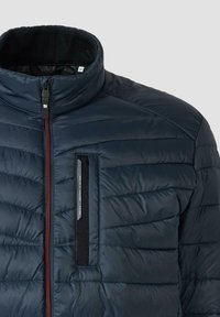 Marineblaue isolierte Puffjacke mit hohem Kragen, Frontreißverschluss und einer Reißverschlusstasche auf der Brust; verfügt über ein gestepptes Muster und dezente rote Akzente.