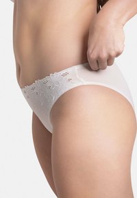 Culotte de bikini blanche avec des détails en dentelle florale à la taille, présentant une texture douce et un design taille basse.