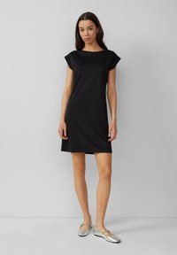 Schwarzes Kurzarmkleid mit Bootsauschnitt, glattem Stoff, knielang, kombiniert mit silbernen flachen Schuhen. Einfaches und zeitgemäßes Design.