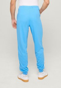 Hellblaue Sweatpants mit elastischem Bund und schmalem Schnitt, aus weichem Stoff. Getragen mit weißen Sneakers und Gummisohle.