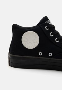 Svart canvas högsko med svarta snören, gummisula och vit emblem som har en stjärna och text på utsidan.