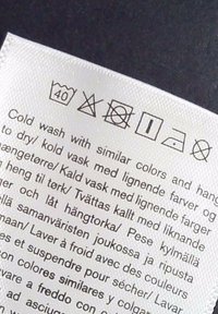 Étiquette de lavage affichant les symboles d’entretien : laver à 40 °C, pas d’eau de javel, ne pas passer au sèche-linge, sécher par égouttage, repasser à basse température, pas de nettoyage à sec, avec instructions multilingues pour lavage à froid.