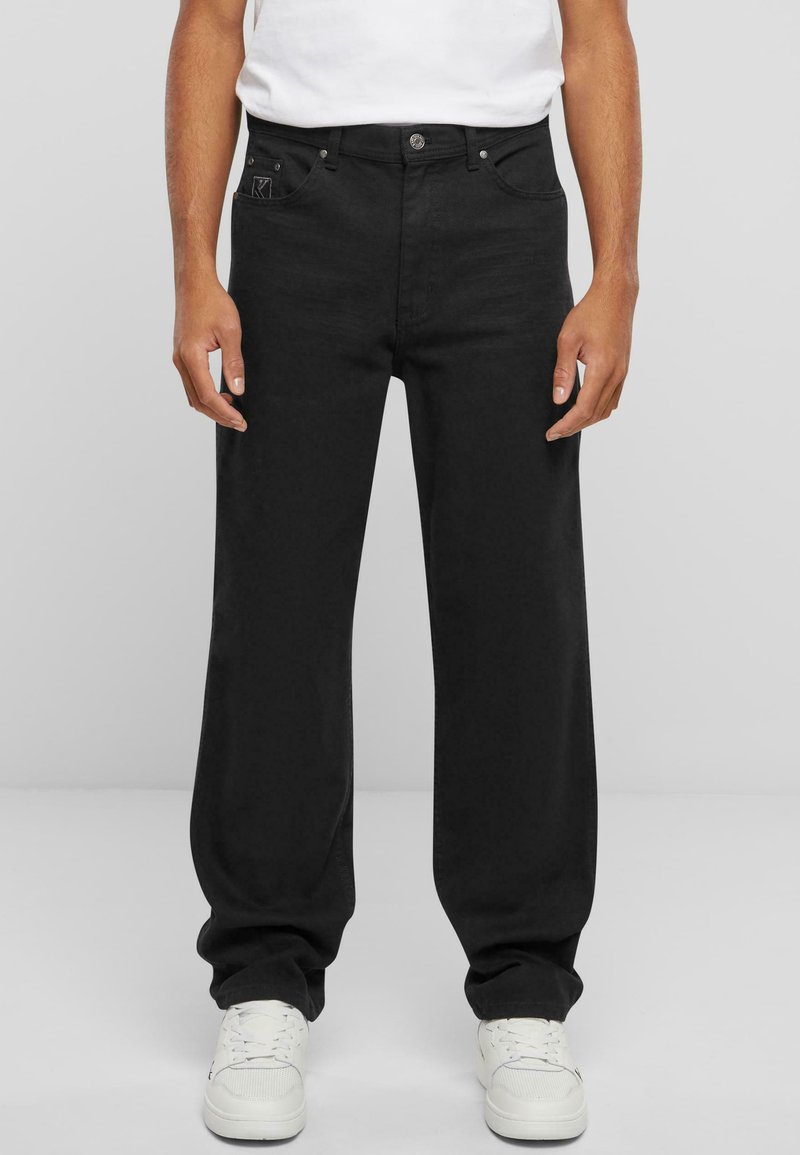 Black straight-leg jeans made of denim, featuring front pockets, a button closure, and subtle logo on the left pocket. Worn with white sneakers.