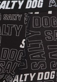 Črne kratke hlače z ponavljajočim se beelim besedilnim vzorcem "SALTY DOG." Elastični pas vsebuje enako beelo besedilo z naglasnim logotipom.