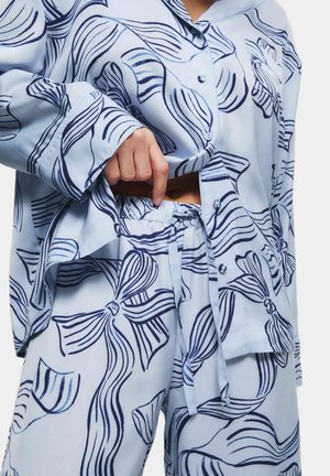 Lichtblauw loungewear-set met een knoopsysteem lange mouwen shirt en broek met trekkoord, versierd met marineblauwe strikpatronen en vloeiende lijnen.