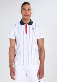 Hvitstripet polo skjorte med marineblå krage og røde knapper. Har en liten logo på brystet og korte ermer. Jevn tekstur.