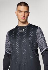 Schwarz, langärmliges Sportshirt mit strukturiertem grauen Muster und Under Armour-Logo auf der Brust. Glattes Material mit kontrastierenden Akzenten.