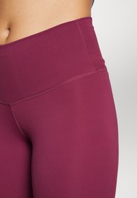 Burgundské legíny s vysokým pasem vyrobené z hladké, elastické tkaniny. Mají ploché švy a široký pas pro pohodlí a oporu.