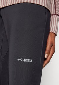 Sorte Columbia Titanium bukser med en glat tekstur og logo detail i hvid, med en tætsiddende design og accent syninger.