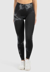 Leggings neri con un design grigio marmorizzato, vita alta, tessuto testurizzato, lunghezza completa, abbinati a scarpe da ginnastica bianche.