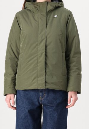 Personne portant une veste d'hiver verte à capuche avec une fermeture éclair avant cachée et un jean bleu, debout les mains détendues le long du corps.