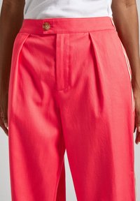 Pantaloni su misura fucsia con pieghe, chiusura a bottone marrone e strisce laterali. Realizzati in tessuto liscio, presentano un design a gamba dritta.