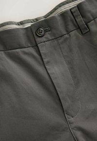Gros plan sur la taille d'un pantalon gris foncé avec fermeture par bouton, passants pour ceinture et détail de couture visible.