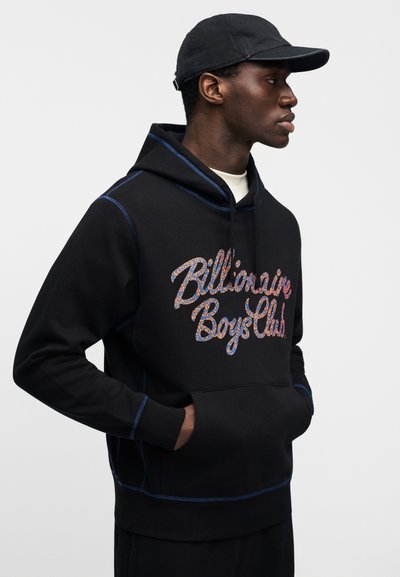 Μαύρο φούτερ με κουκούλα και μπλε ραφές, με πολύχρωμο λογότυπο "Billionaire Boys Club" σε καλλιγραφική γραφή. Φορεμένο με μαύρο καπέλο.