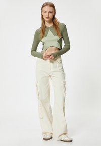 Sudadera corta verde con diseño de estrellas; combinada con pantalones cargo de pierna ancha color crema con bolsillos laterales y acentos de costura amarilla.