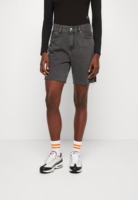 Džínové šortky v tmavě šedé barvě s třepeným lemem. Kombinované s černým dlouhým rukávem a černobílými teniskami s oranžovými akcenty.