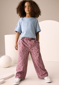 Maglietta a maniche corte azzurro chiaro abbinata a pantaloni larghi con stampa floreale rosa e sneakers bianche, su uno sfondo semplice.