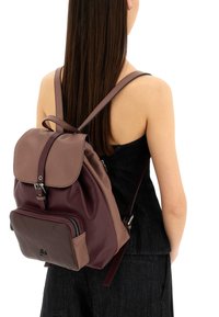 Zaino in pelle marrone con chiusura a pattina, spallacci regolabili, tasca frontale con zip e finitura testurizzata. Design multicolore in marrone scuro e chiaro.