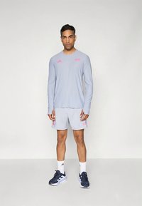 Heledat hall pikkade varrukatega särk ja sobivad lühikesed püksid roosade aktsentidega, tehtud siledast materjalist. Mustad sportkingad siniste triipudega.