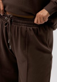 Braune Baumwoll-Sweatpants mit elastischem Bund und verstellbarem Kordelzug, ausgestattet mit Seitentaschen und einem weichen, strukturierten Stoff.