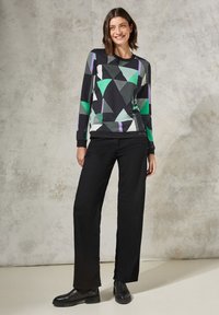 Maglia a maniche lunghe con una base nera decorata con motivi geometrici verde, turchese e viola. Abbinata a pantaloni larghi neri e stivaletti alla caviglia.