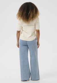 Top lavorato a maglia di colore crema con maniche corte, caratterizzato da motivi orizzontali testurizzati; abbinato a jeans a gamba larga di colore blu chiaro.