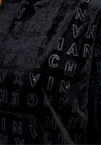 Tela de terciopelo negro con letras en relieve de diferentes tamaños. La textura parece suave con un brillo sutil, mostrando un diseño sin costuras.
