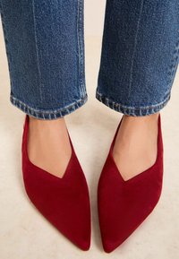 Balerini roșii din velur cu vârf ascuțit și design cu tăietură în V, asortați cu blugi cropped din denim albastru. Textură netedă și siluetă elegantă.