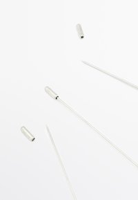 Ensemble d'aiguilles en métal de différentes longueurs, de couleur argentée, avec des pointes aiguisées et des capsules cylindriques argentées, disposées sur un fond blanc.
