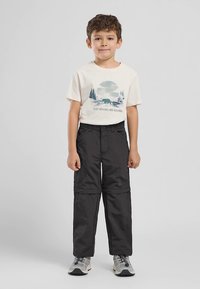 Juodos atsegamos kelnes su lygiu paviršiumi, derinamos su kremine marškinėlių su meškos ir miško grafika. Pilki sportbačiai užbaigia aprangą.