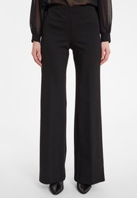 Zwarte wijde broek met een gestructureerde afwerking en subtiele glans. Elastische tailleband, vloeiende uitstraling en lange silhouette voor een comfortabele pasvorm.