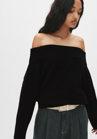 Czarny sweter typu off-the-shoulder z szerokim ściągaczem na dekolcie, noszony na szarej spódnicy z wysokim stanem, uzupełniony jasnym paskiem.